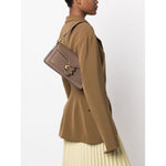 Person wearing Coach Tabby 26 leather shoulder bag with adjustable strap, featuring a brown jacket and pleated skirt.