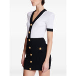 Model wearing Balmain Two-tone twisted knit bodycon dress with V-neck and gold buttons, showcasing white and black color scheme.