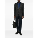 Model wearing a blue Brunello Cucinelli Cashmere zip-up sweatshirt under a gray blazer, paired with black trousers and holding a bag.