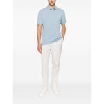 Brunello Cucinelli Polo shirt with embroidery in light blue with short sleeves, button placket, and logo detail, worn with white pants.