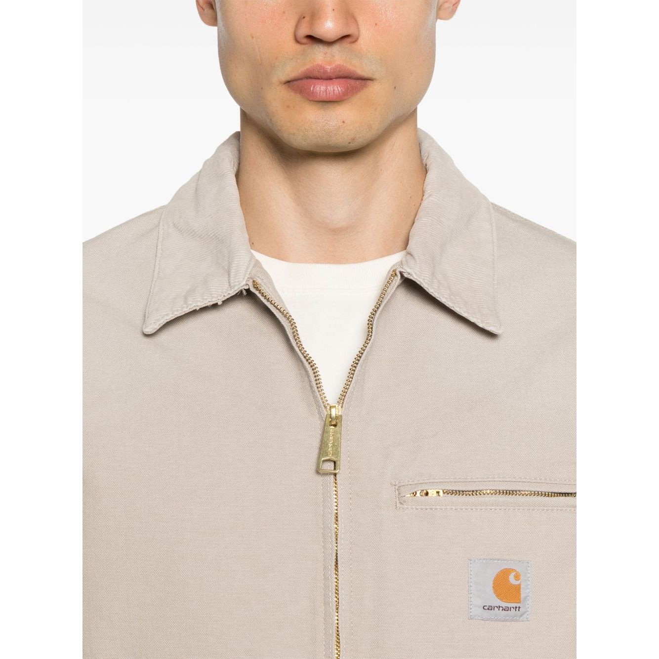 Man wearing CARHARTT WIP MAIN Jackets Beige with zip fastening and chest pocket, showing front design.