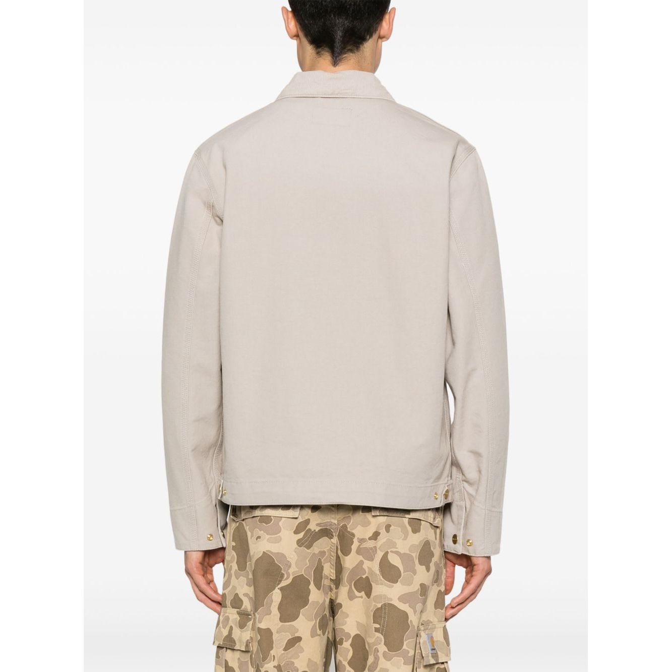 Back view of CARHARTT WIP MAIN Jackets Beige, canvas jacket with press-stud cuffs, worn with camo pants.