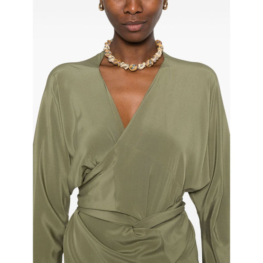 Model wearing olive green Cortana Cortana Serp Silk Jumpsuit with V-neck and tied waist, showcasing long sleeves and draped design.