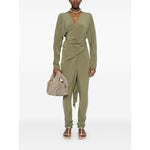 Model wearing Cortana Cortana Serp Silk Jumpsuit, olive green tied waist V-neck design with long sleeves, accessorized with a beige bag.