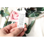 Close-up of label on Dolce & Gabbana White Floral Silk One Shoulder Midi Dress, highlighting floral pattern and care instructions.