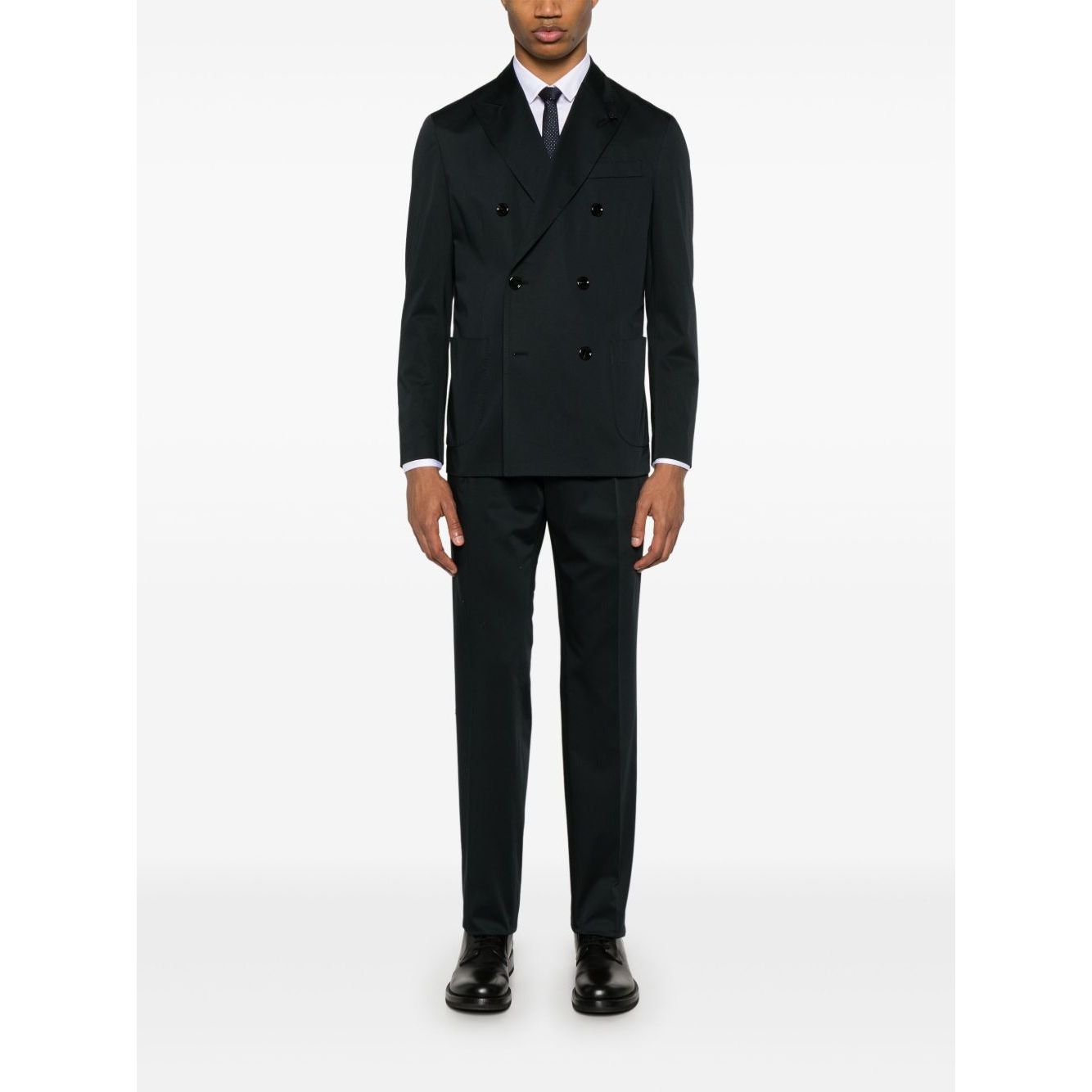 Man wearing a black double-breasted suit with a tie and dress shoes standing against a white background