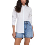 Woman wearing Jacqueline De Yong Blue Cotton Shirt with long sleeves, paired with denim shorts, showcasing versatile fashion.