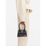 Jacquemus Le Chiquito Moyen Black Bag with gold hardware and removable strap, held by model, stylish Italian design, 18x13.5 cm.