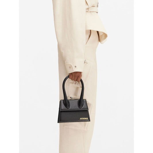 Jacquemus Le Chiquito Moyen Black Bag with gold hardware and removable strap, held by model, stylish Italian design, 18x13.5 cm.