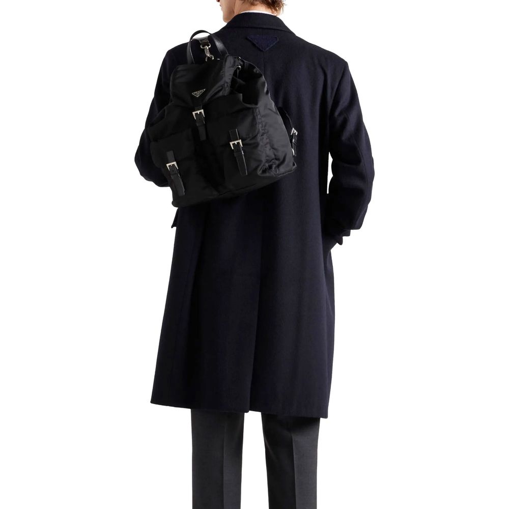 Man wearing Prada Blue Wool Coat with black backpack, showing back triangle logo detail, long sleeves, and straight hemline, made in Italy.