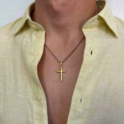 Gold cross necklace worn with an open yellow shirt, displaying elegance and simplicity.