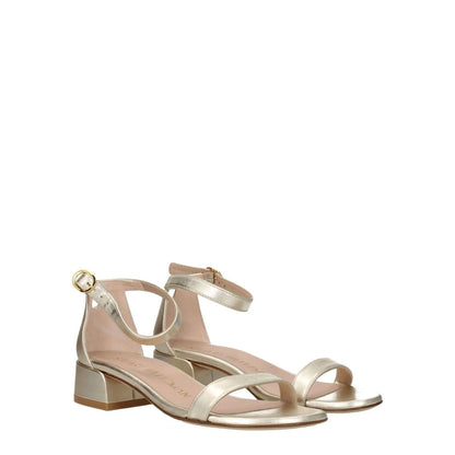 Stuart Weitzman Gold Leather Sandals with buckle closure and open toe, featuring a mid heel and metallic platinum finish.