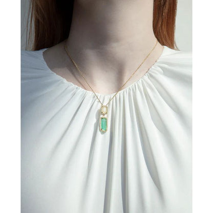 Woman wearing a gold necklace with a green pendant in a white blouse.