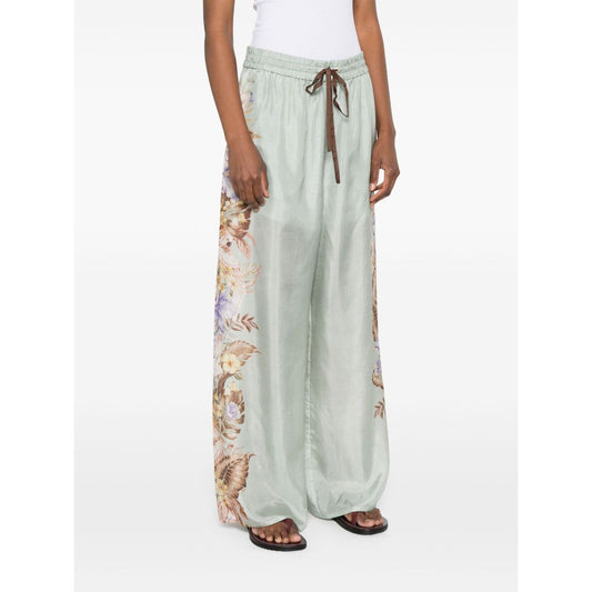 Woman wearing Zimmermann Coco trousers featuring a sage green floral print with elasticated drawstring waistband and side pockets.