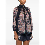 Woman wearing a Zimmermann Rhiannon Billow blouse featuring a navy blue paisley print, long sleeves, and front button fastening.