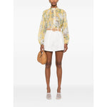Model wearing Zimmermann Shorts Ivory with a high-waisted design, belt loops, and side slit pockets, paired with a floral blouse.